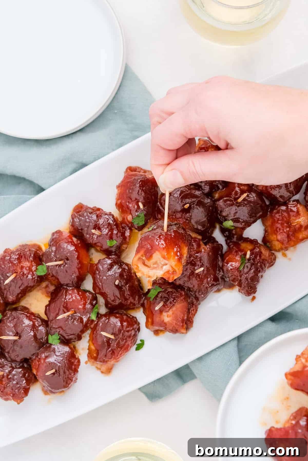 A hand reaching to take a delicious bacon-wrapped water chestnut from a white serving plate, highlighting its finger-food appeal.