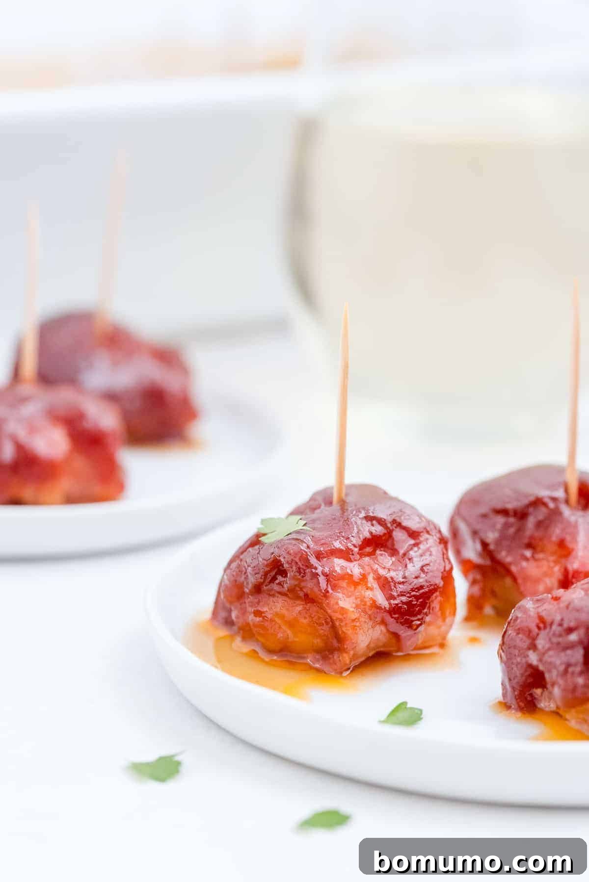 A perfectly cooked bacon-wrapped water chestnut, gleaming with sauce, resting on a white plate among others, ready for serving.