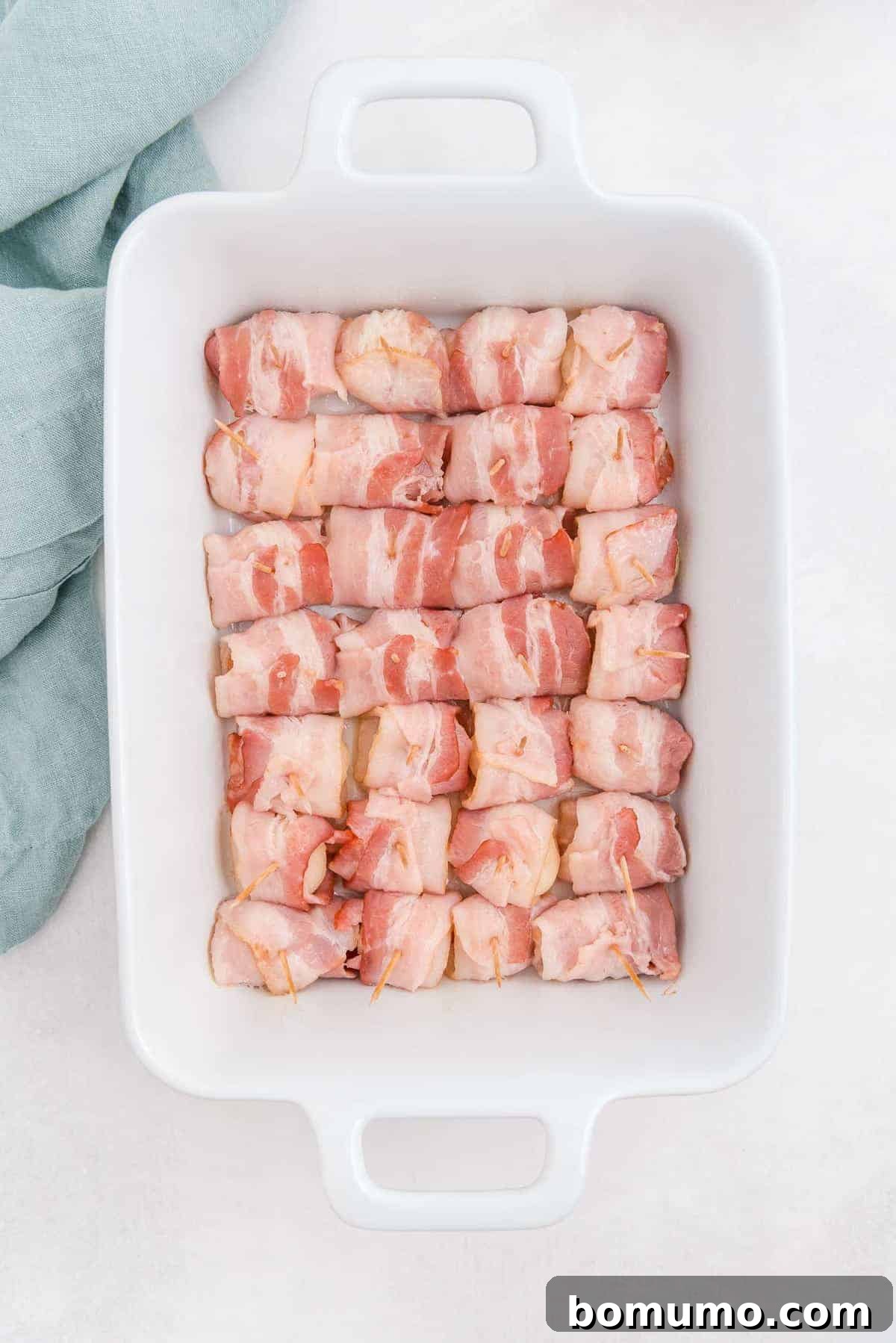 A baking dish filled with partially cooked bacon-wrapped water chestnuts, the bacon just beginning to brown and crisp up.