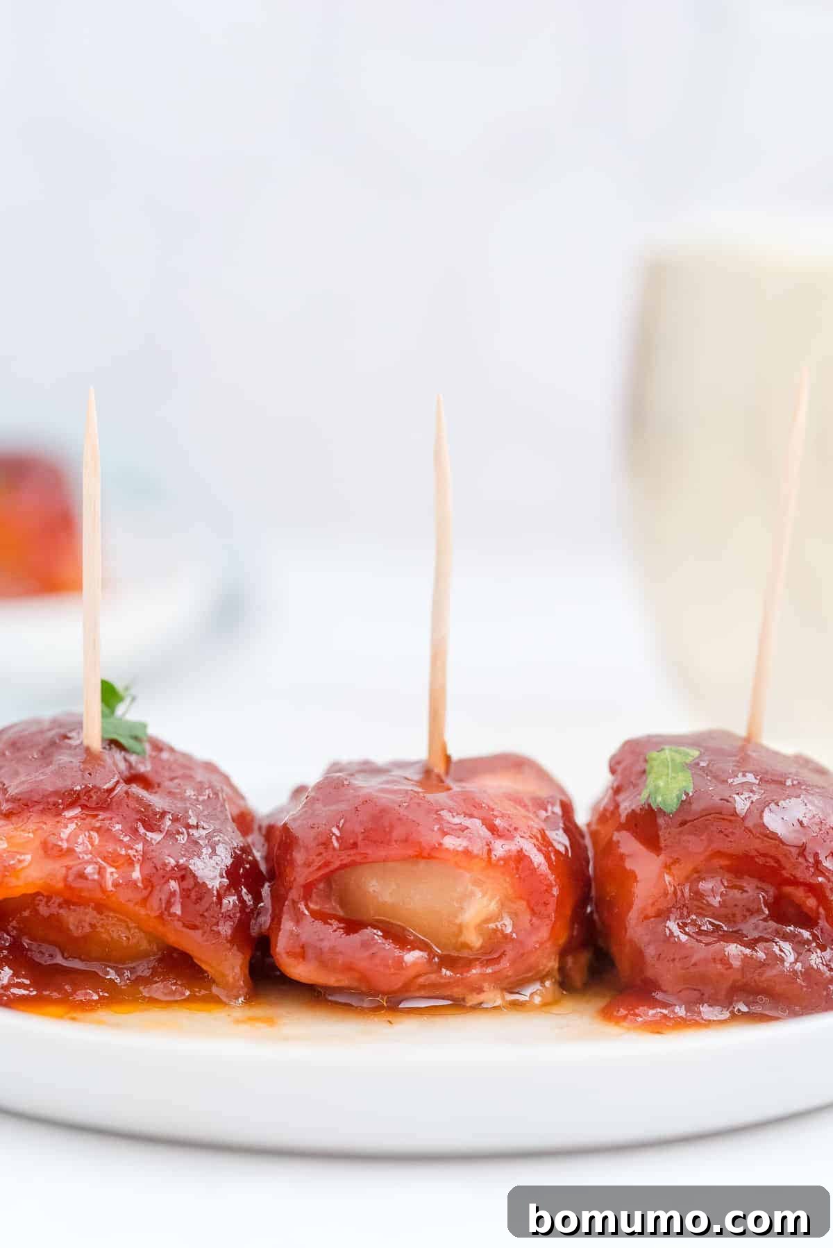 Three perfectly sauced and glistening bacon-wrapped water chestnuts arranged appealingly on a simple white plate, ready for serving.