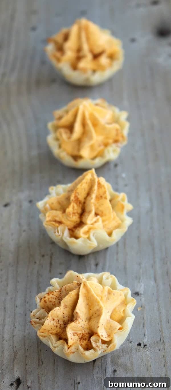 These bite-sized pumpkin pie tarts are a quick and easy no-bake treat and a delicious addition to a Thanksgiving dessert table! A row of mini pumpkin pie tarts elegantly arranged on a rustic wooden table, ready for a fall gathering.