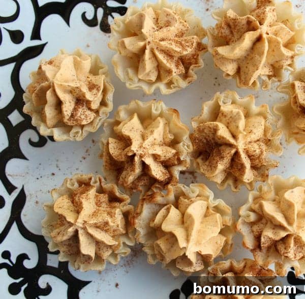 These bite-sized pumpkin pie tarts are a quick and easy no-bake treat and a delicious addition to a Thanksgiving dessert table! An inviting overhead view of mini pumpkin pie tarts, garnished with a sprinkle of spice, on a clean countertop.