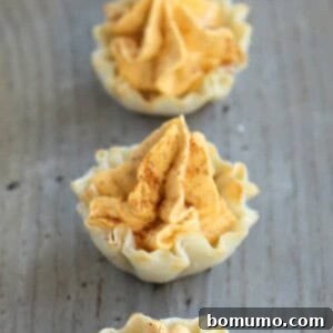 A row of mini pumpkin pie tarts on a wooden table, featuring a perfect bite-sized presentation.