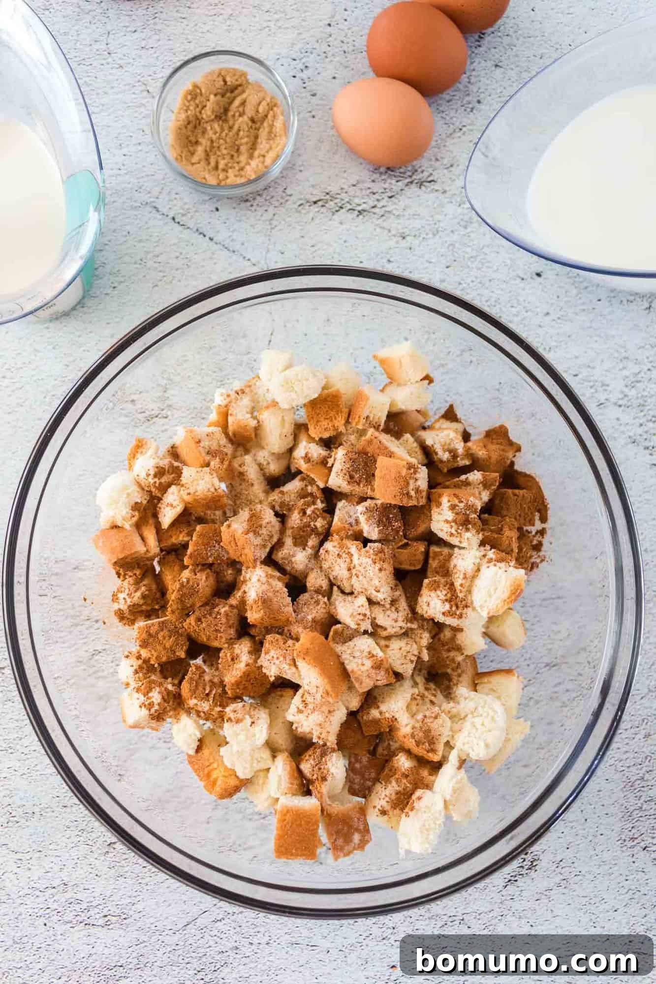 Close-up shot of bread cubes lightly dusted with ground cinnamon and nutmeg in a mixing bowl.