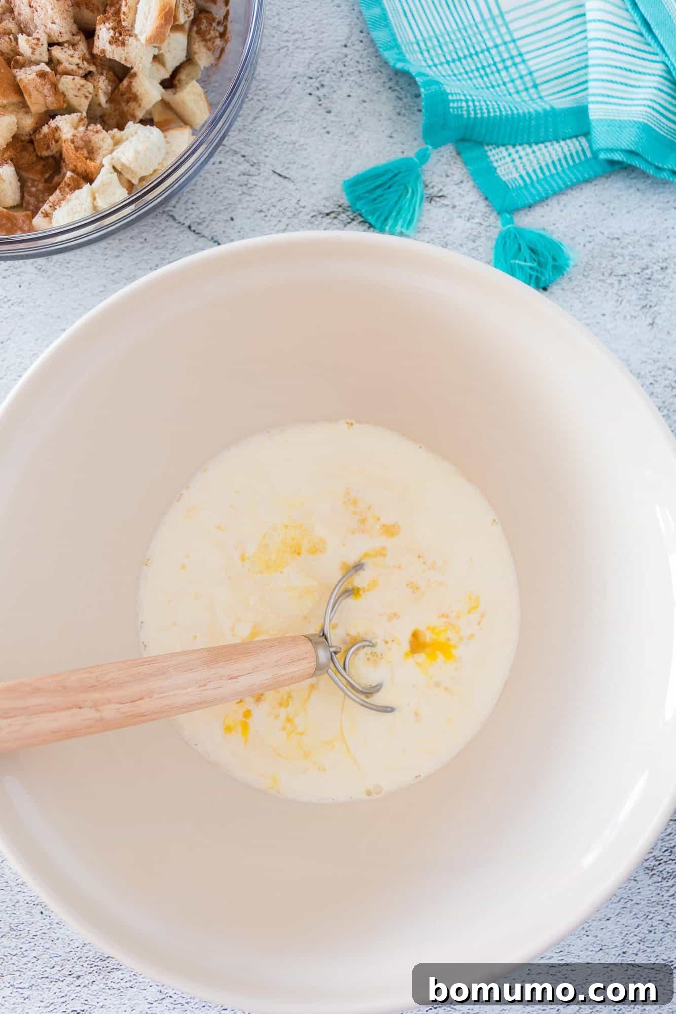 A whisk blending eggs and brown sugar in a large bowl, forming the base of the French toast custard.