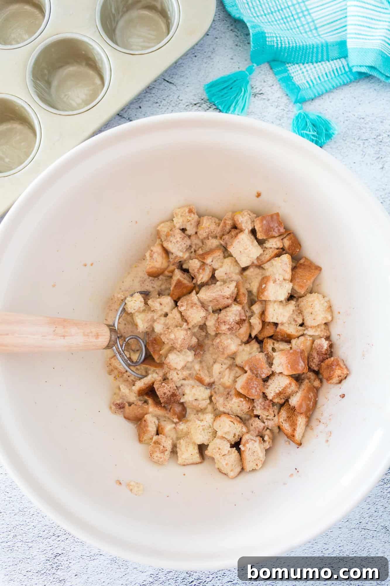 Cubed bread being gently folded into the rich custard mixture, ensuring even coating.