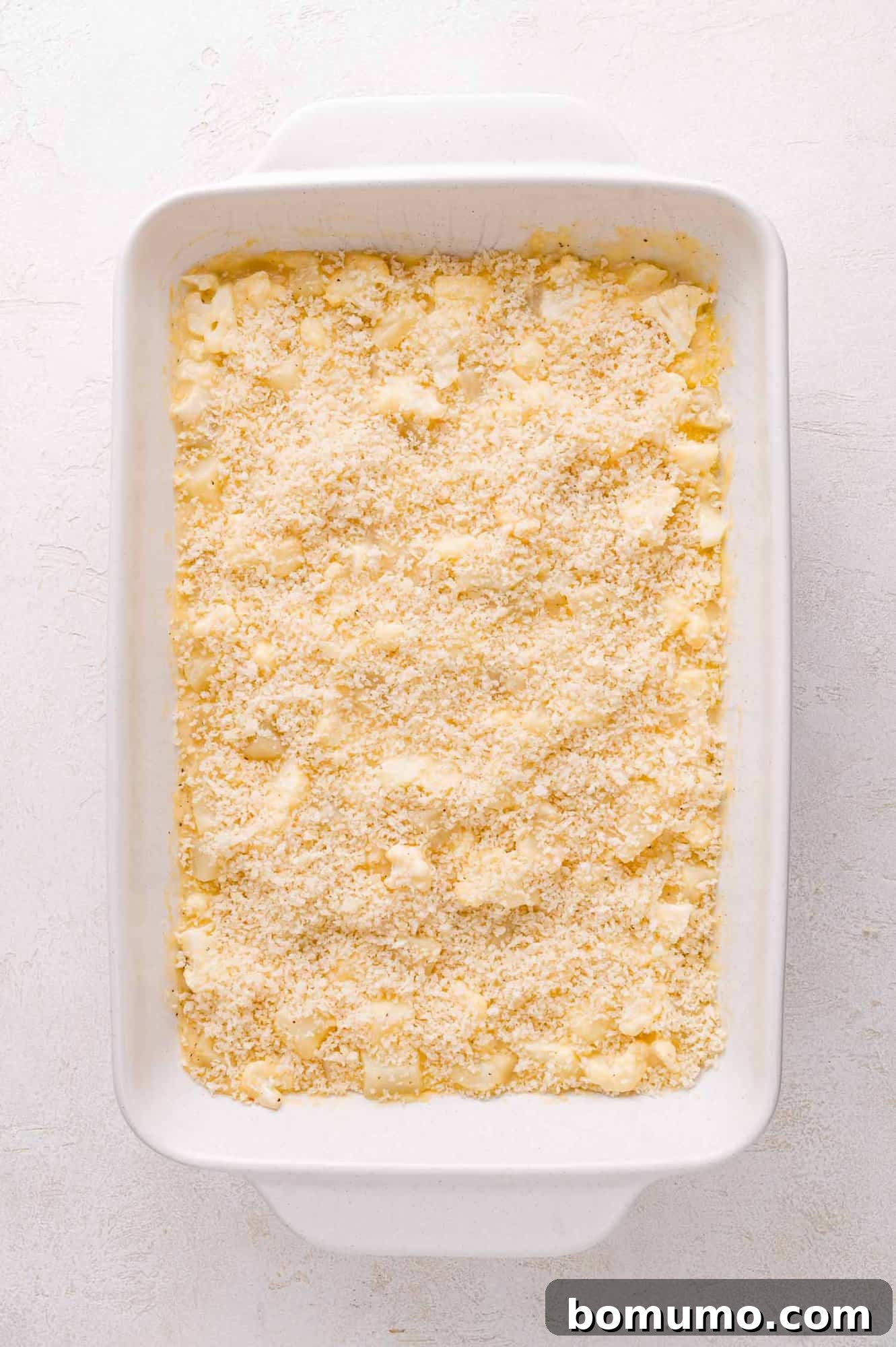 A rectangular white baking dish filled with an unbaked casserole, beautifully topped with a golden layer of seasoned breadcrumbs, ready for the oven.