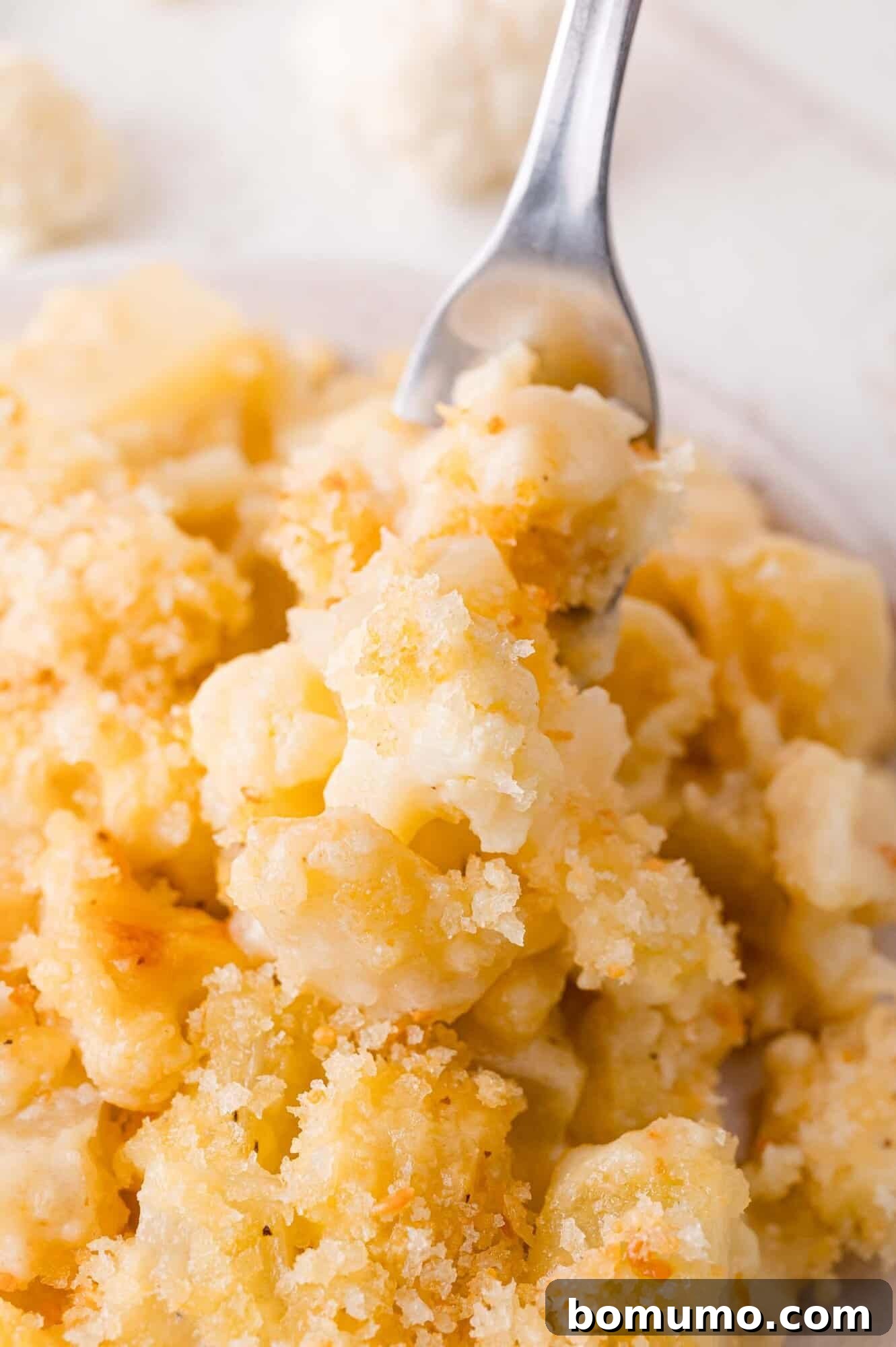 Close-up of baked cauliflower and potato casserole with a golden breadcrumb topping, with a fork lifting a portion, ready to be enjoyed.