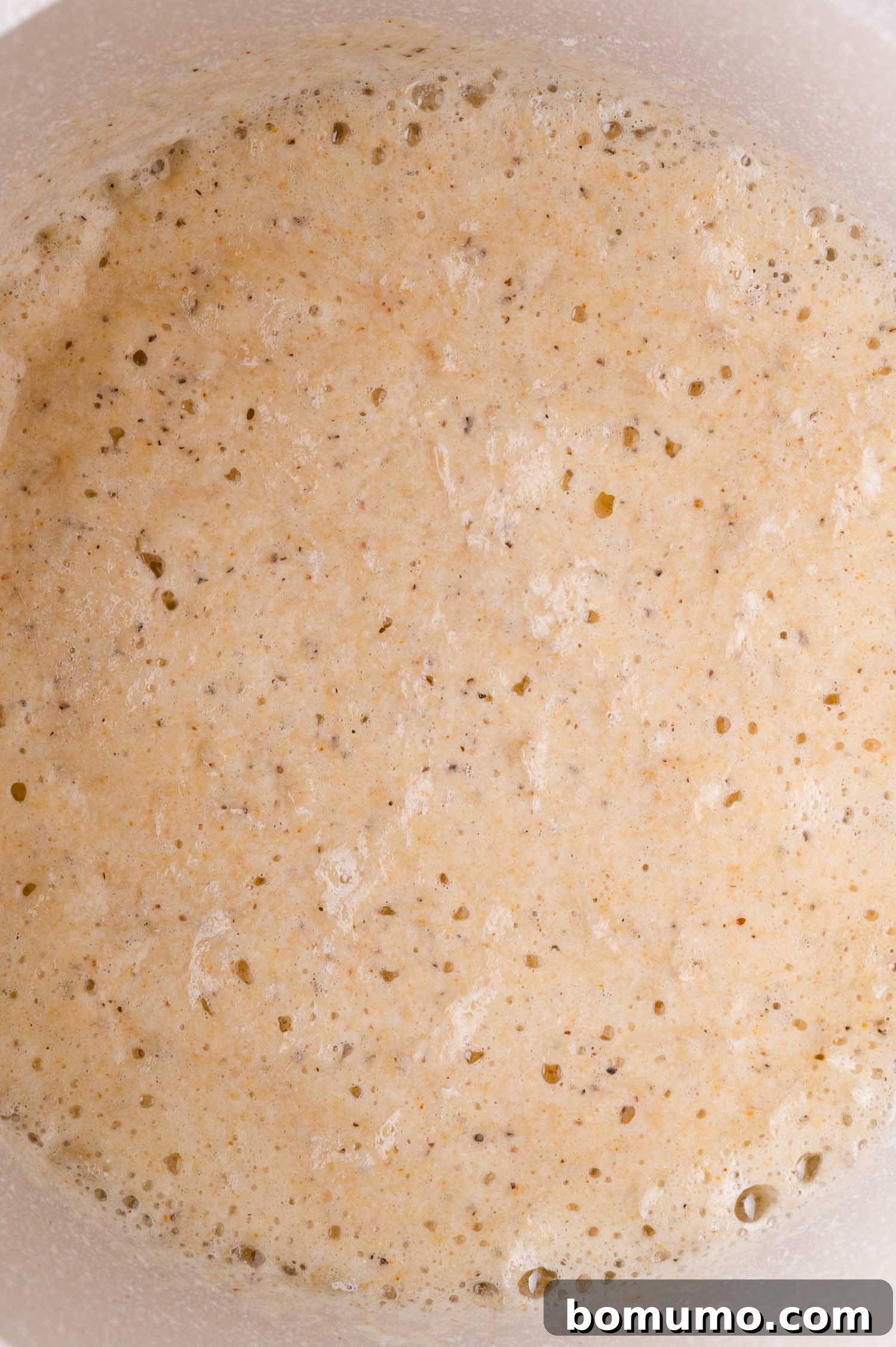 A bubbly, light brown mixture of butter and flour (a roux) cooking in a saucepan, a key step for thickening the cheese sauce.