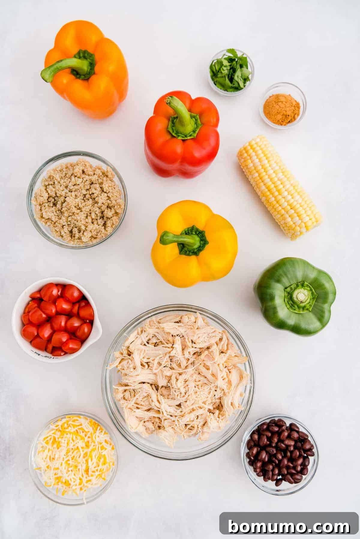 Overhead view of all the fresh and prepared ingredients neatly laid out on a countertop, including whole bell peppers, cooked chicken, black beans, corn, tomatoes, cilantro, and cheese, ready for assembly.