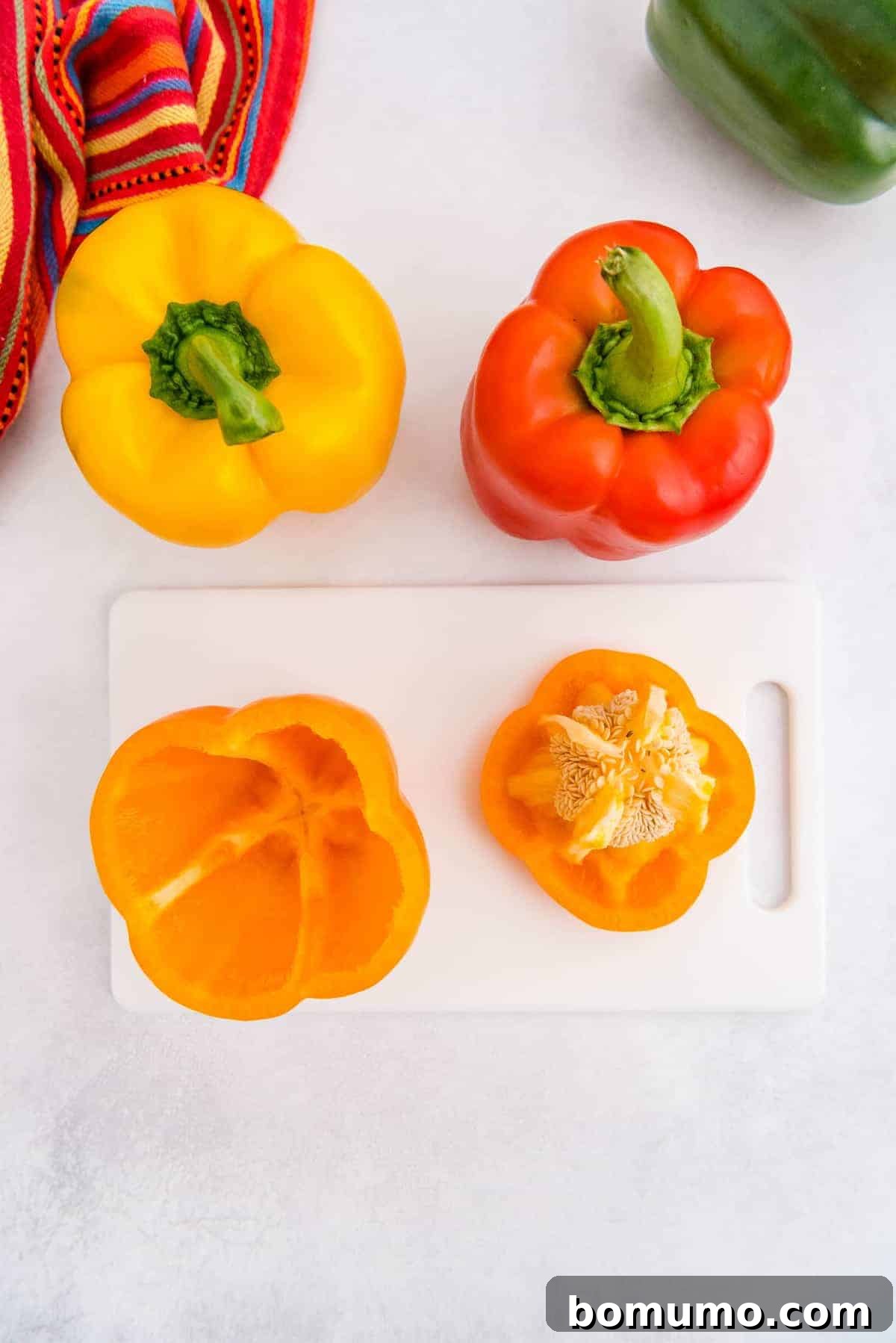 A cook's hands carefully cutting the top off a bell pepper and scooping out the seeds and core, preparing it for stuffing.