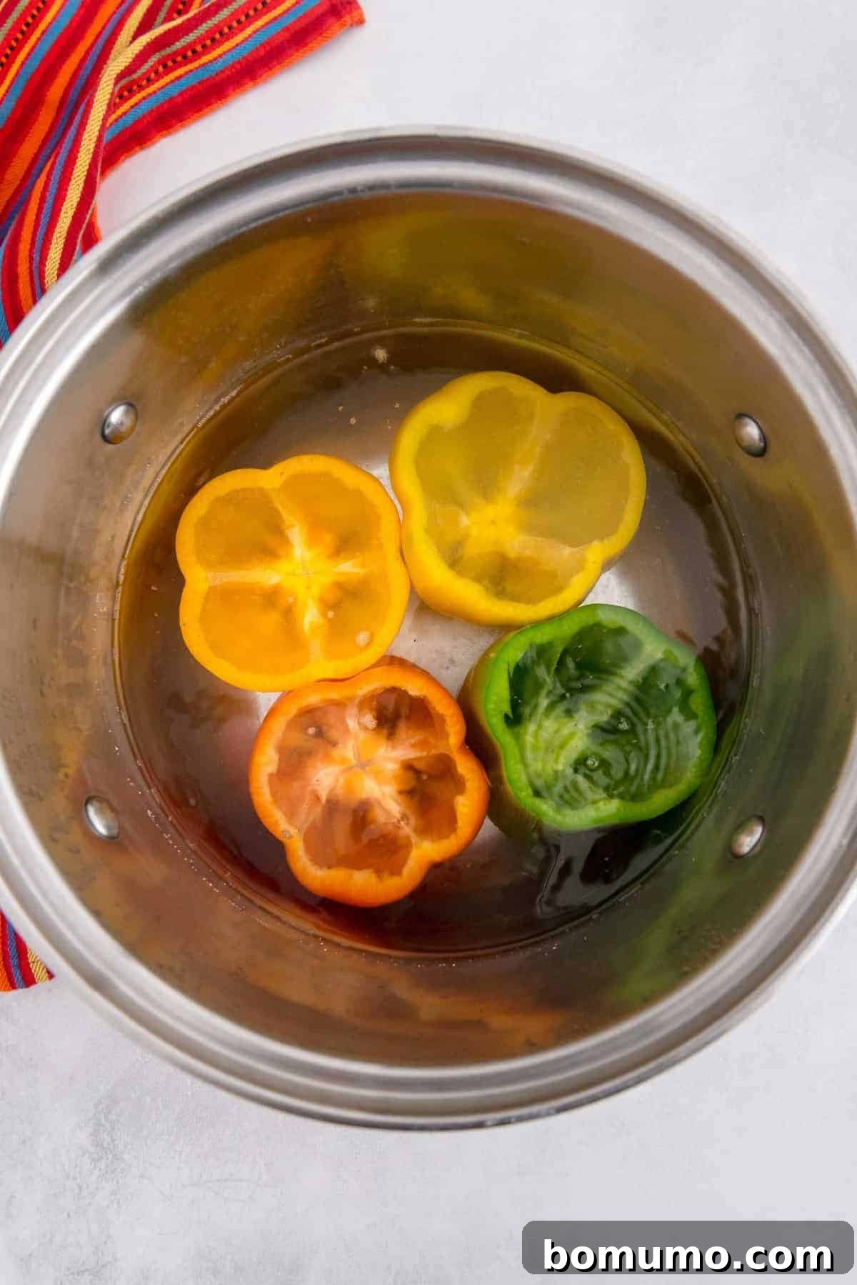 Several bell peppers submerged in a large pot of boiling water, gently blanching to soften their texture before being filled.