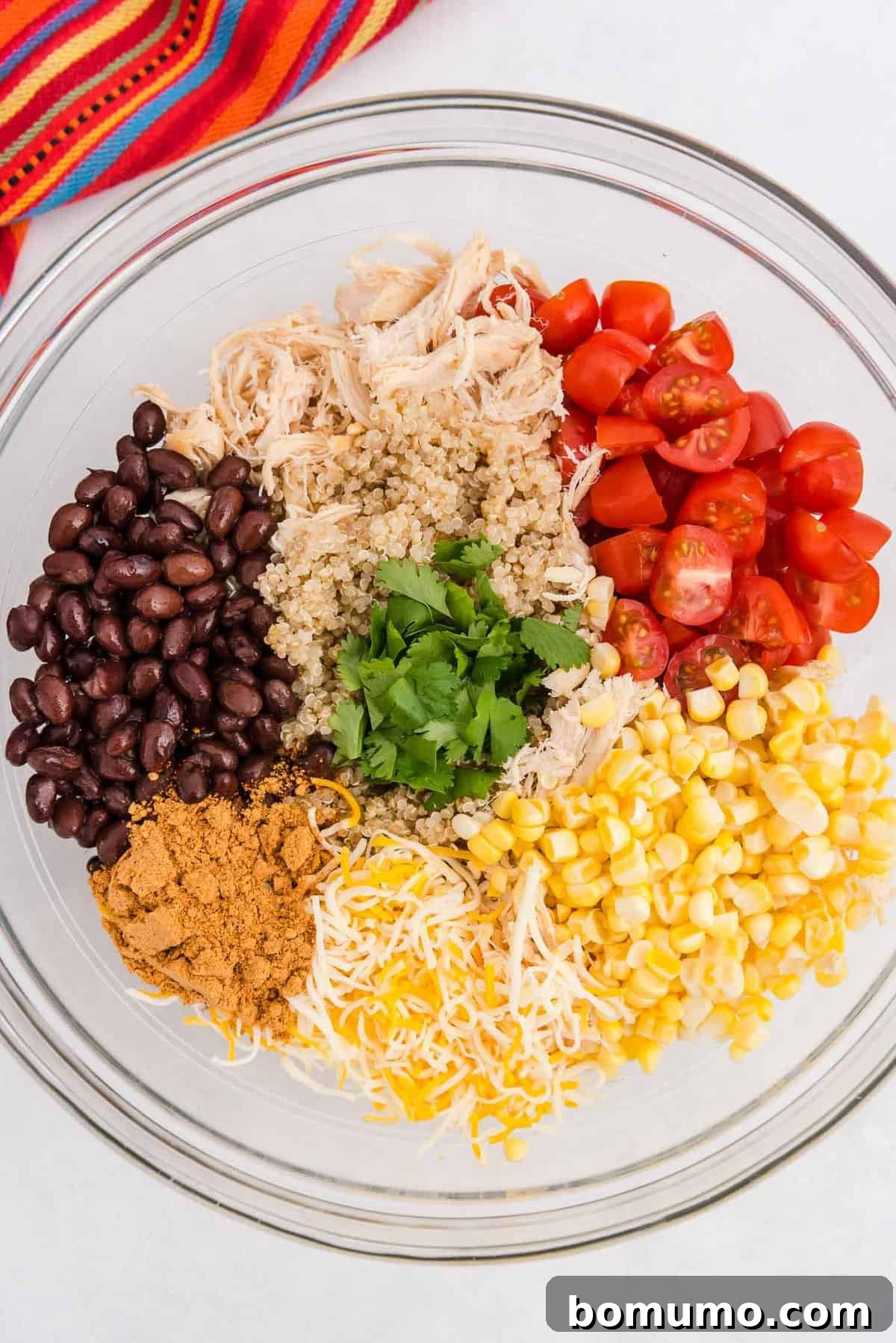 A large glass bowl filled with a colorful and hearty mix of quinoa, shredded chicken, black beans, corn, tomatoes, and other Southwestern ingredients, ready to be combined into a savory stuffing.