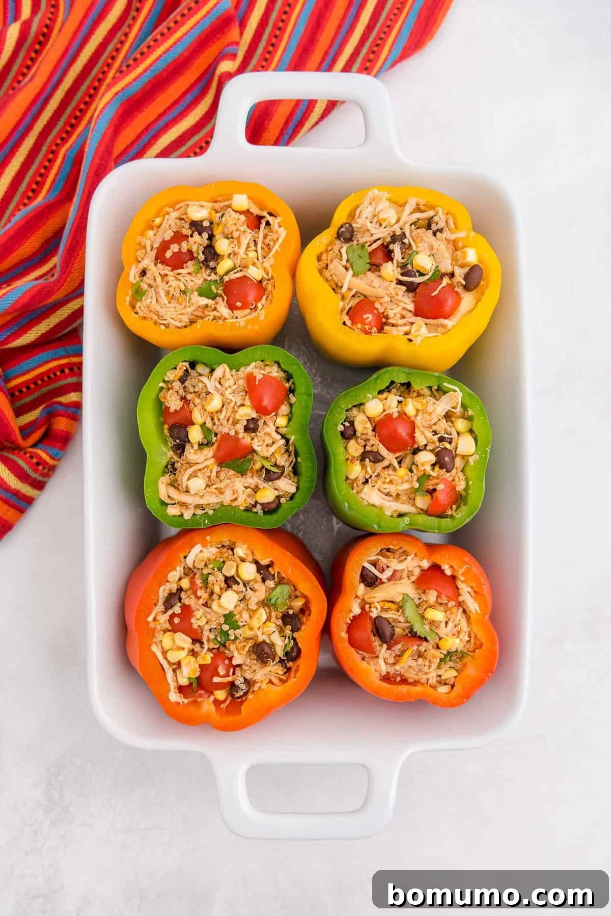 Six bell peppers, brightly colored and generously filled with the Southwestern quinoa and chicken stuffing, arranged in a baking dish and ready for the oven.
