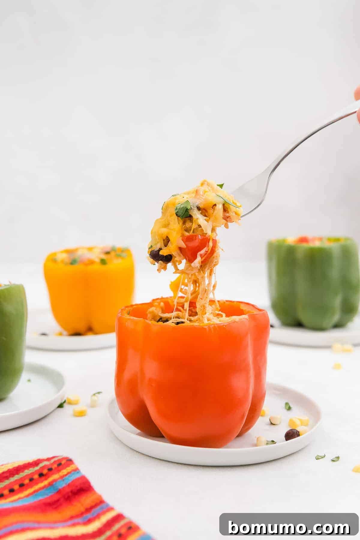 A fork pulling out a spoonful of rich, savory filling from a baked Southwestern stuffed pepper, with other perfectly cooked peppers visible in the background.