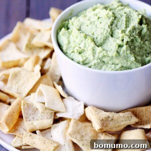 Closeup view of light green dip in a white bowl, surrounded by pita chips.