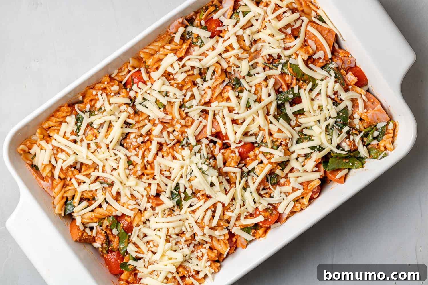 A pristine, unbaked pizza pasta casserole neatly arranged in a baking dish, topped with a generous layer of mozzarella cheese, poised for baking.