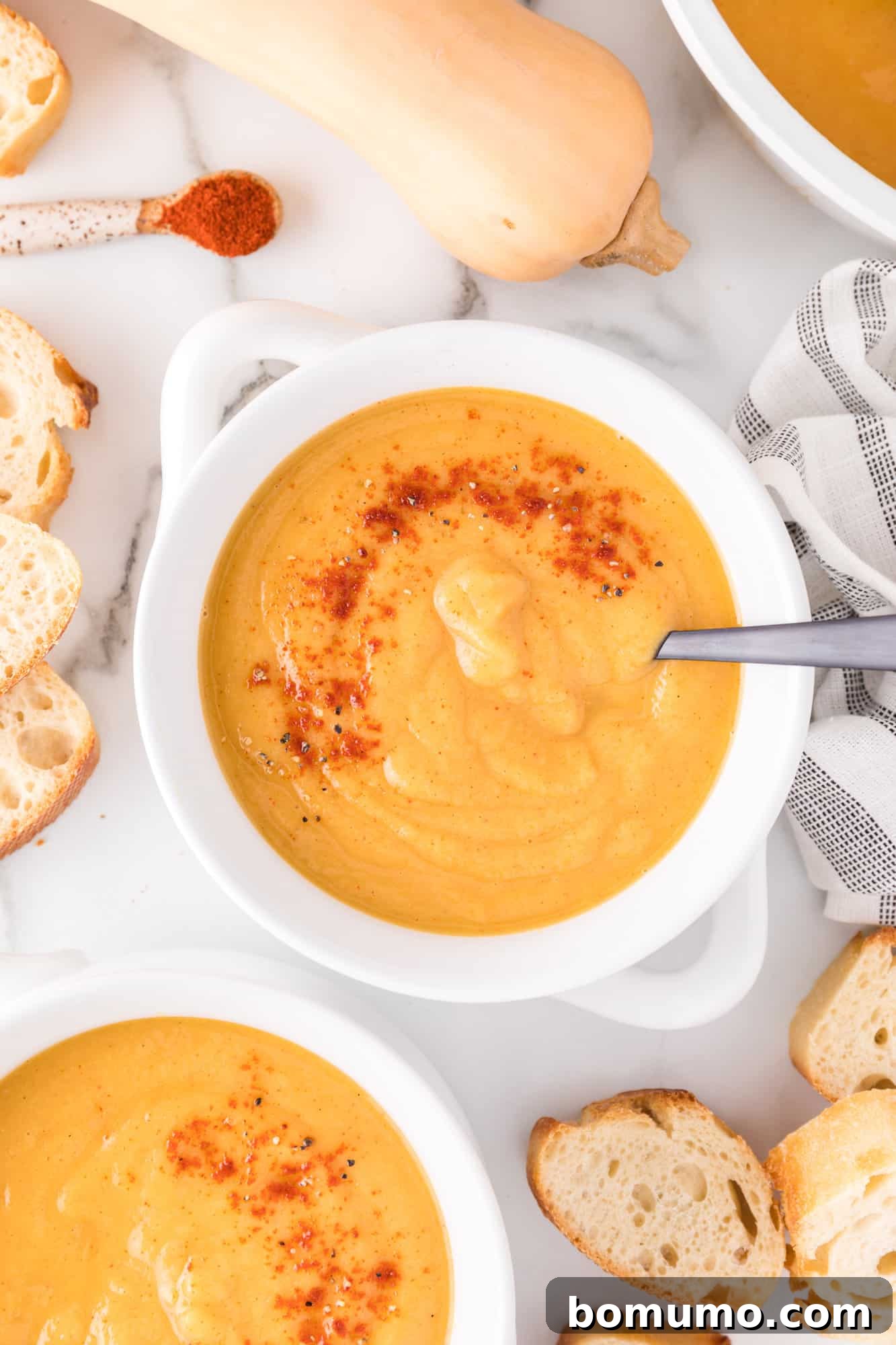 Vegan butternut squash soup in a white bowl, elegantly garnished with a sprinkle of smoked paprika.