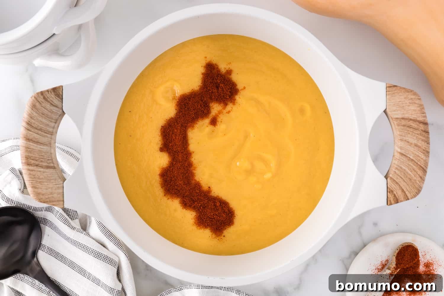 Smoked paprika being stirred into the butternut squash soup in a saucepan.