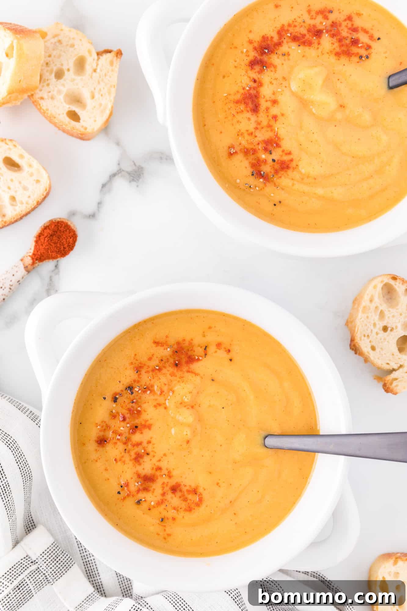 A serving of vegan butternut squash soup garnished with vibrant smoked paprika in a white bowl.