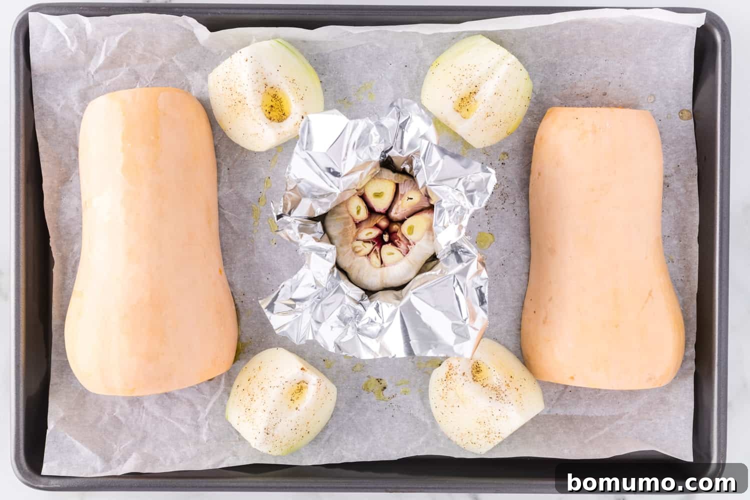 Butternut squash, quartered onion, and foil-wrapped garlic on a baking sheet, ready for roasting.