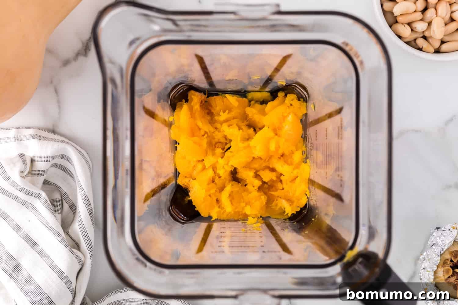 Scooped butternut squash flesh being added to a blender for puréeing.