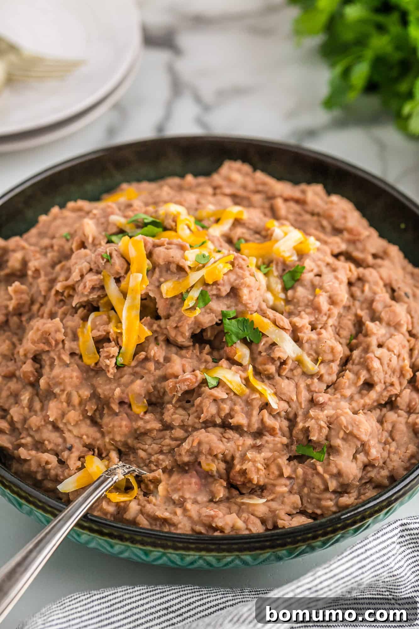 Crockpot refried beans topped with melted cheese and fresh cilantro, ready to be served.