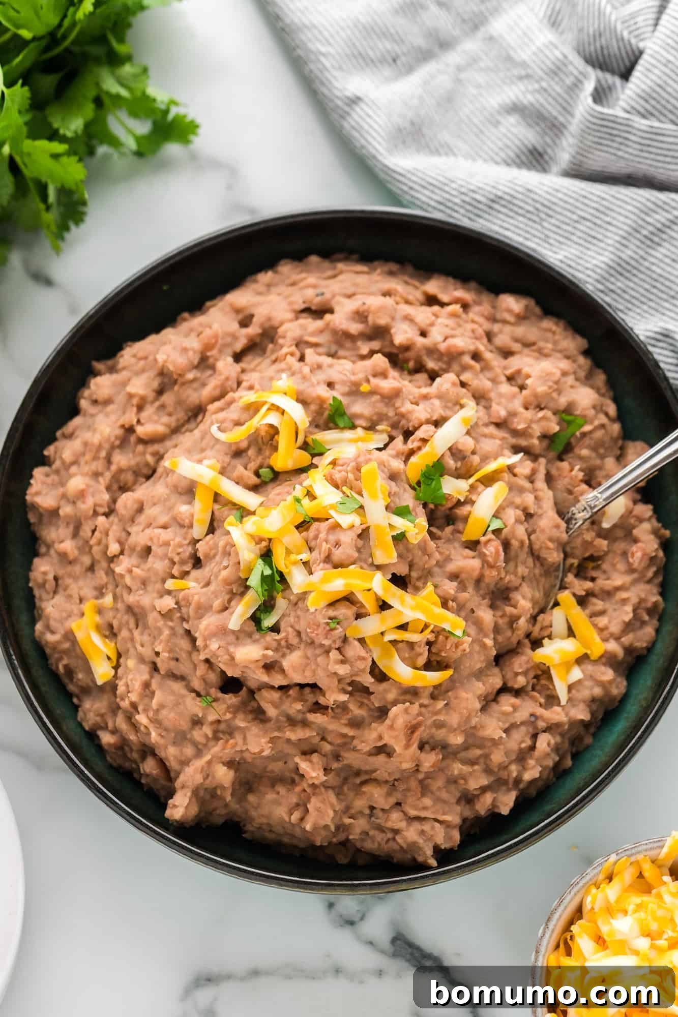 An inviting overhead view of a large bowl of homemade crockpot refried beans, generously topped with shredded cheese and fresh cilantro, ready to be enjoyed.