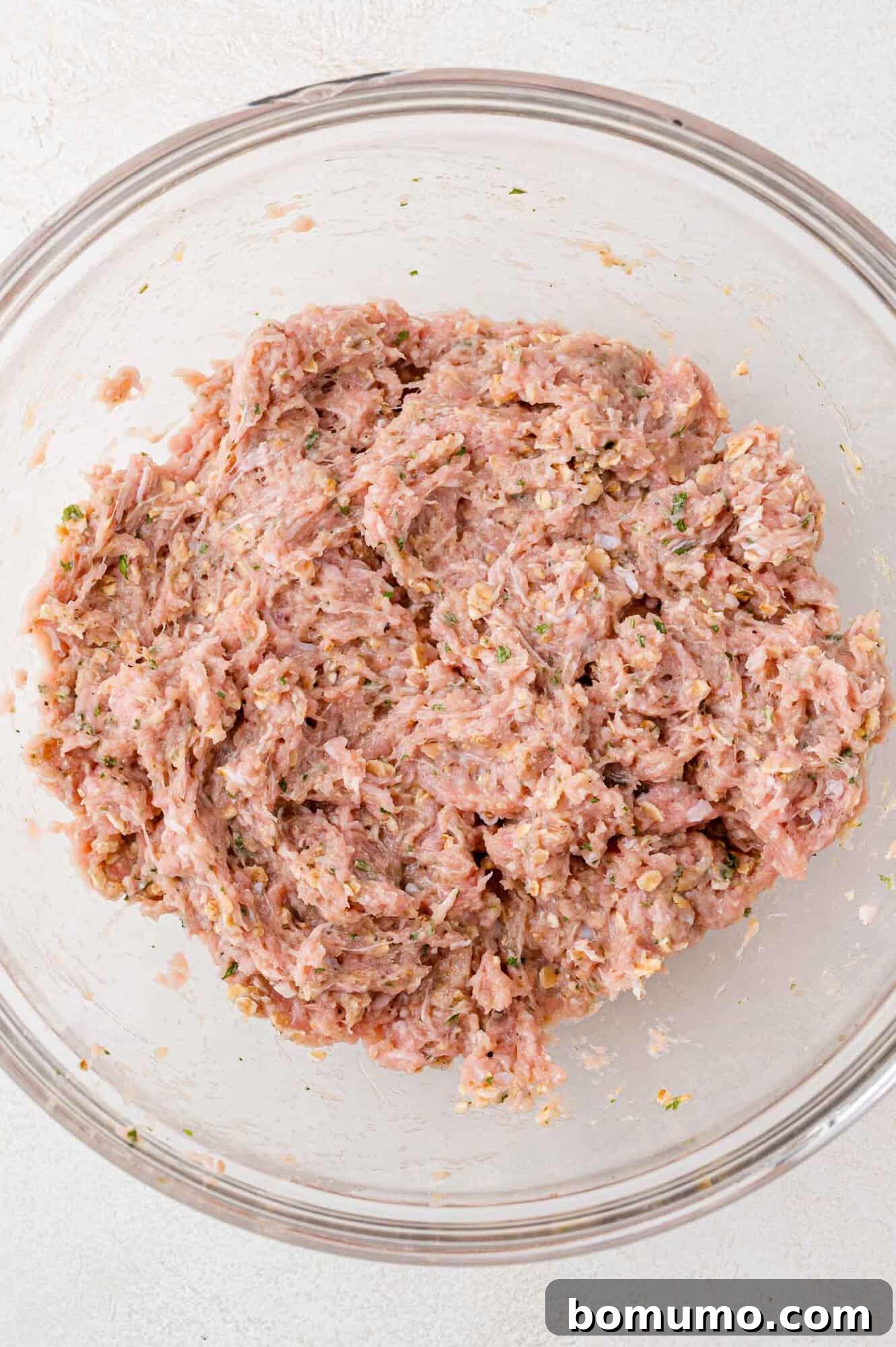 A close-up shot of a glass bowl filled with a thoroughly mixed blend of ground turkey and aromatic spices, showcasing the even distribution of ingredients.