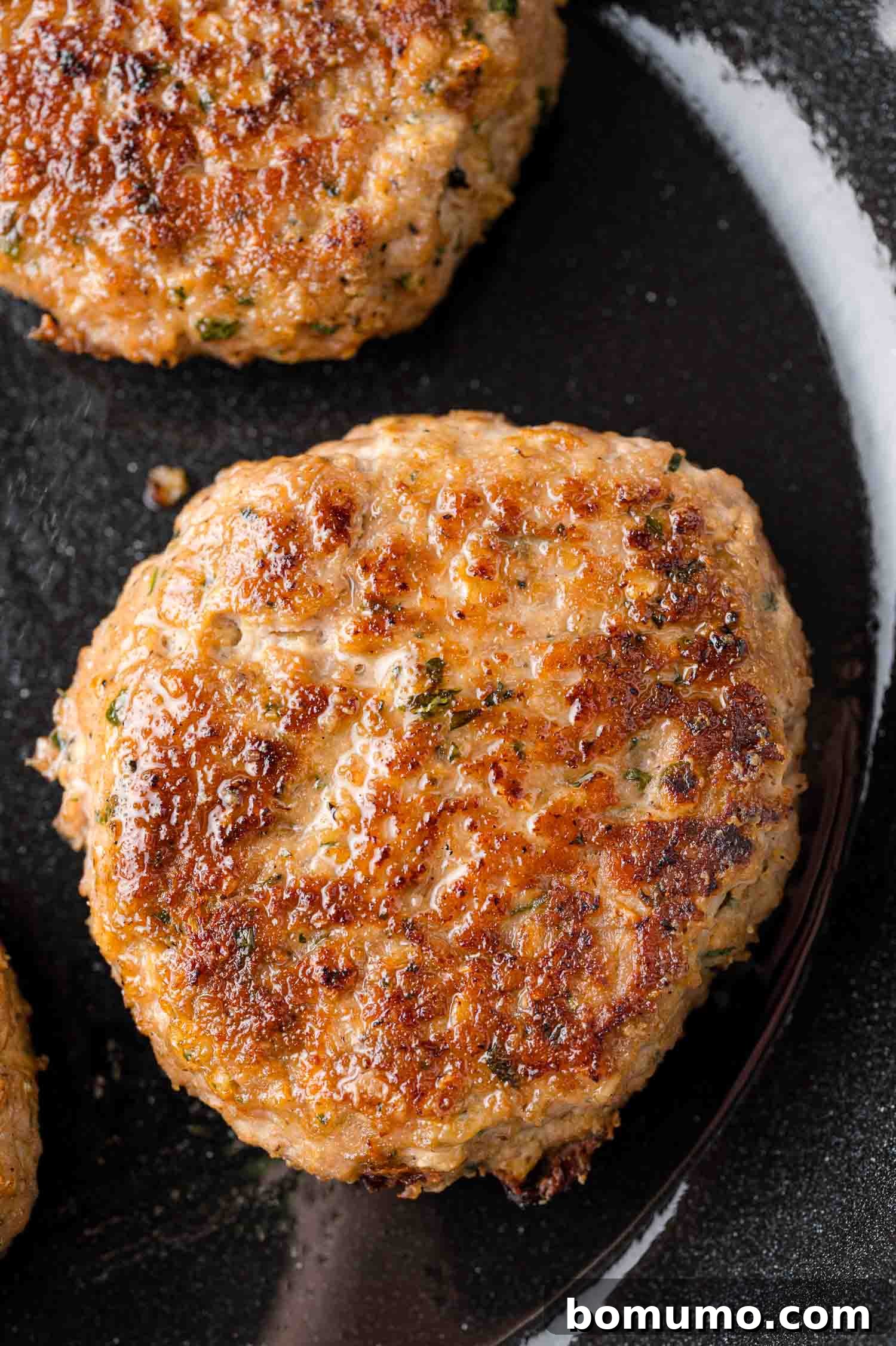 A close-up view of two perfectly browned, cooked turkey burger patties resting on a sleek black surface, highlighting their appealing texture.