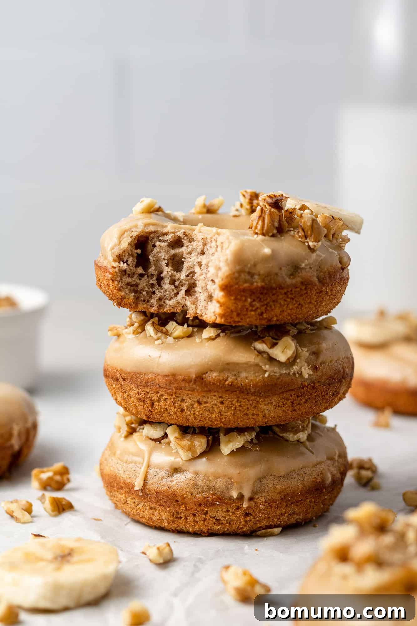 A stack of three baked banana donuts with a bite taken out of the top one, showcasing the soft texture.