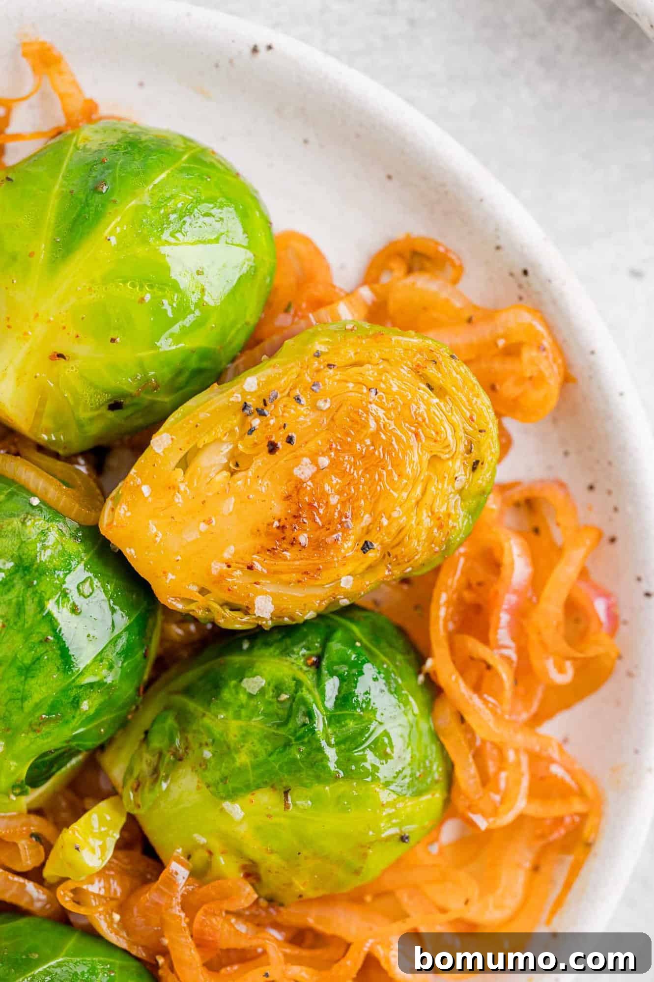 Close-up of perfectly cooked Brussels sprouts halves mixed with sautéed shallots in a pan.