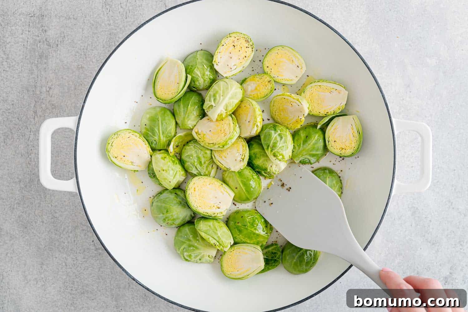 Brussels sprouts steaming in a white frying pan with a little water, covered.