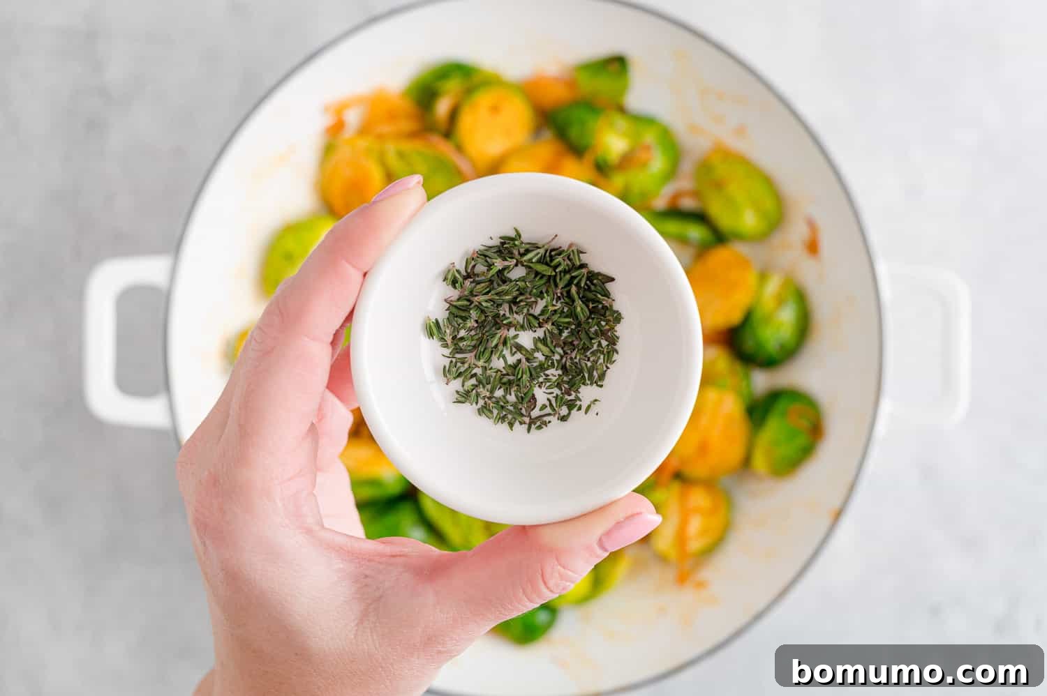Fresh thyme leaves being sprinkled over the hot, sautéed Brussels sprouts just before serving.