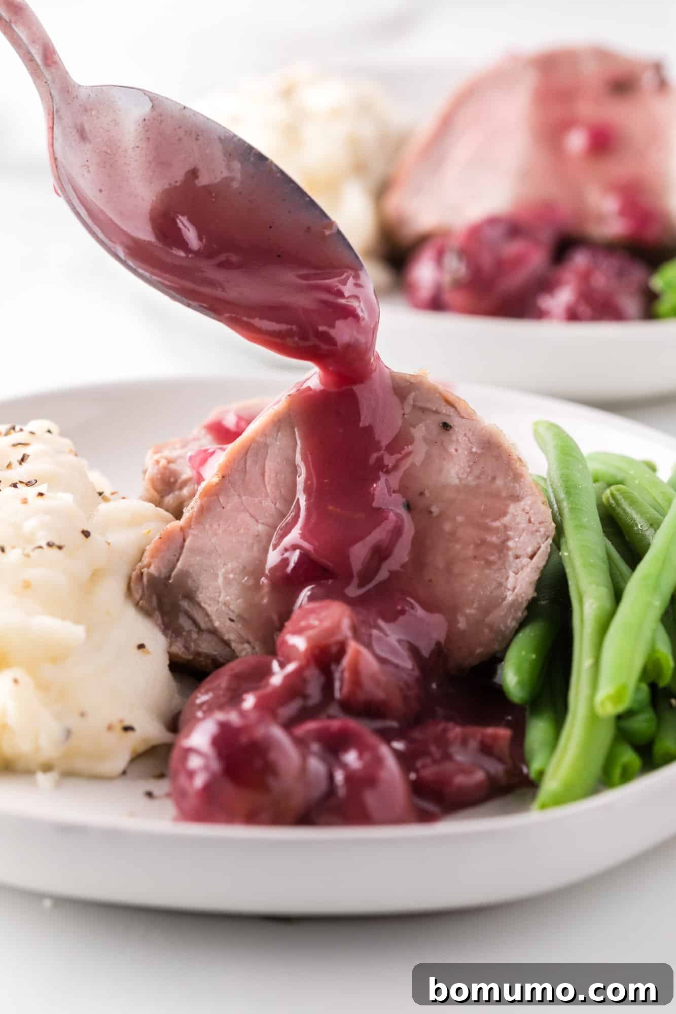 Slices of perfectly cooked pork tenderloin being generously topped with a rich port wine and roasted grape sauce.