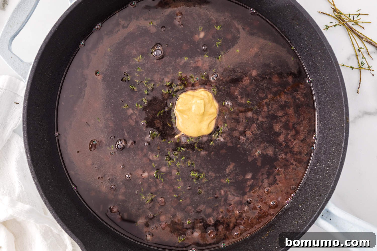 Dijon mustard being stirred into the simmering port wine and shallot mixture to enhance flavor and aid thickening.