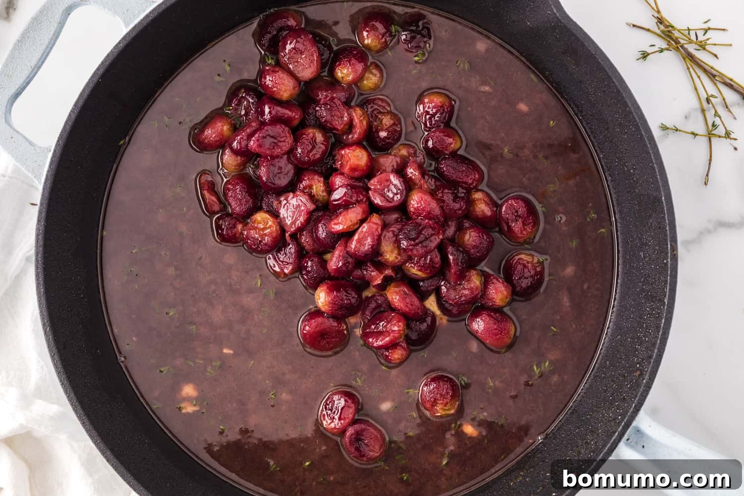 Roasted grapes being gently folded into the simmering port wine sauce, adding sweetness and texture.