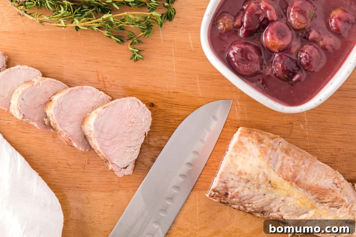 A sharp knife slicing a rested pork tenderloin into thick, juicy medallions.