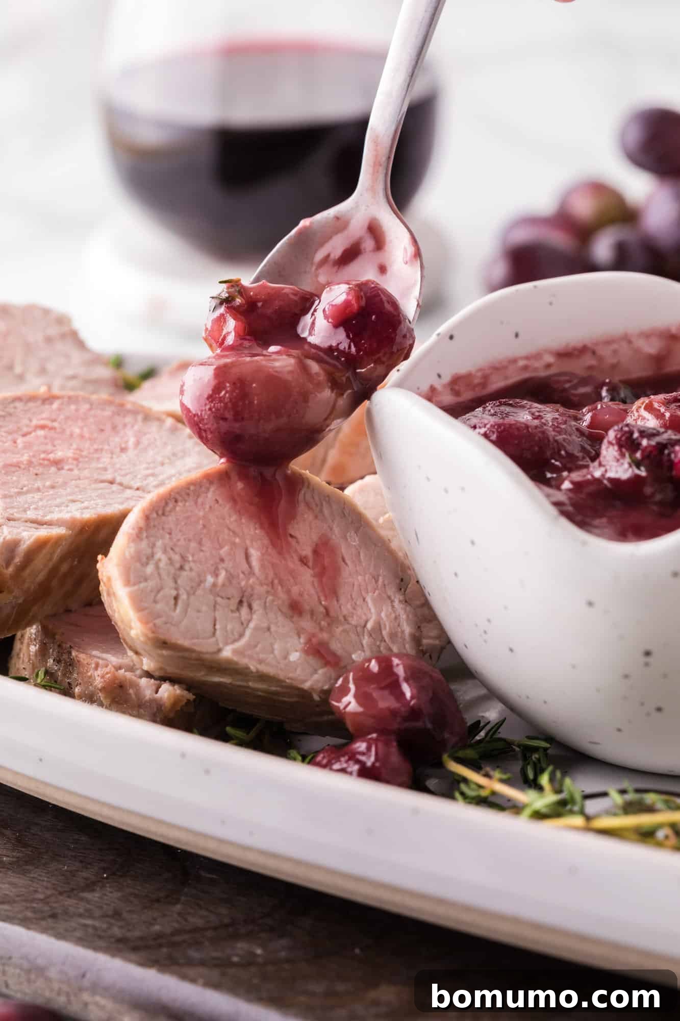 Rich port wine sauce, laden with tender roasted grapes, being drizzled over perfectly sliced pork tenderloin on a serving plate.