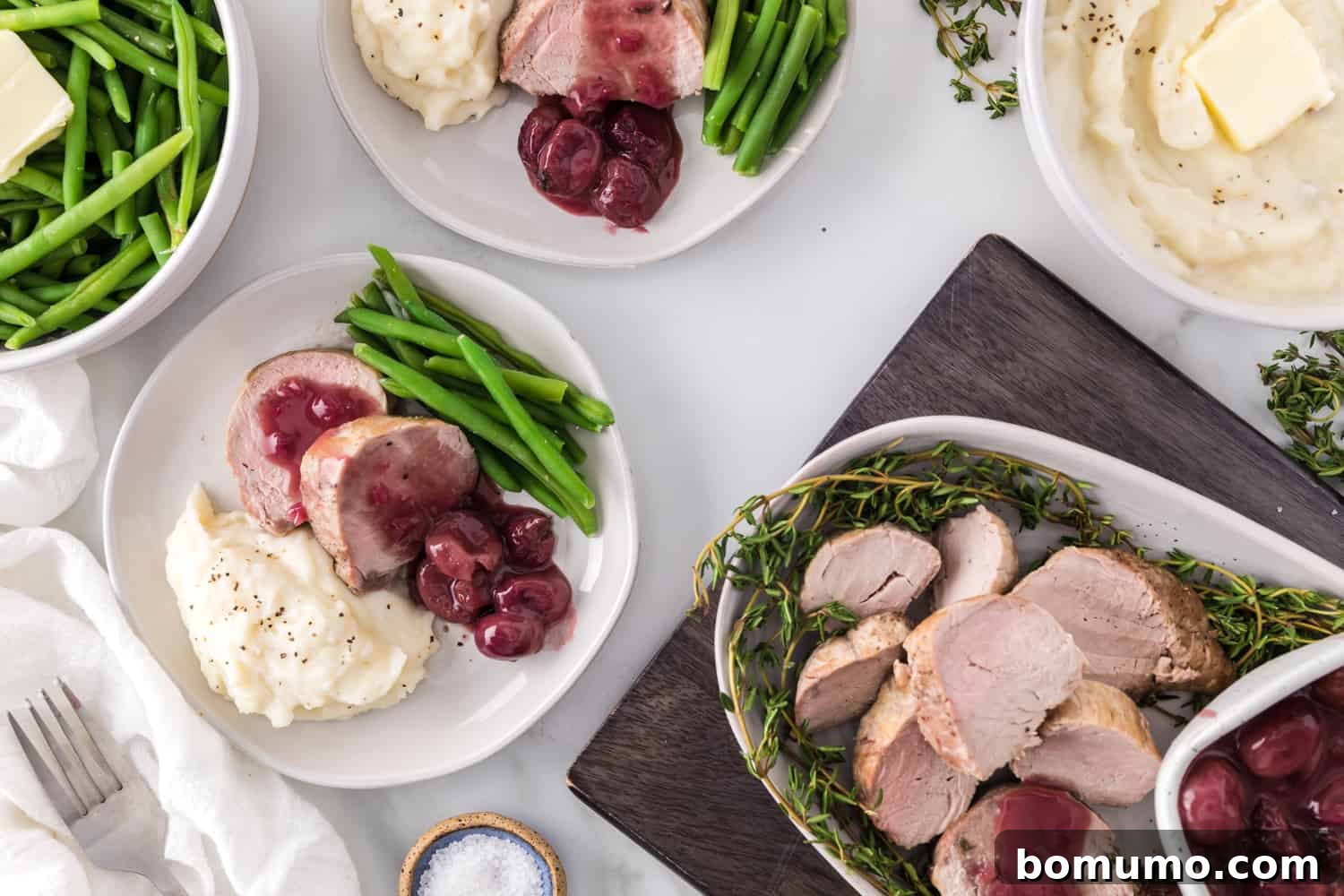 An overhead view of a plated meal featuring sliced pork tenderloin with port wine sauce, roasted grapes, and a selection of colorful side dishes.