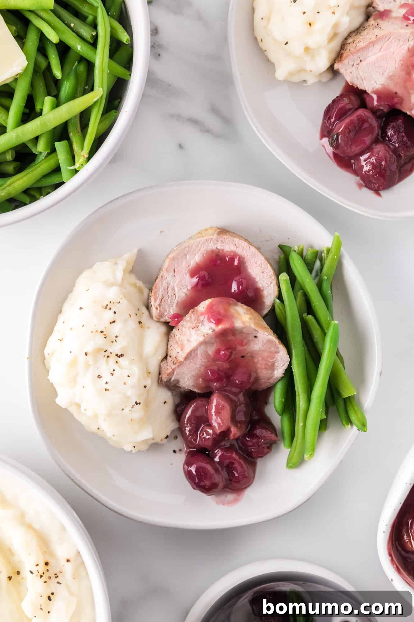 A beautifully plated dish featuring sliced pork tenderloin, rich port wine sauce with roasted grapes, alongside vibrant green beans and creamy mashed potatoes.