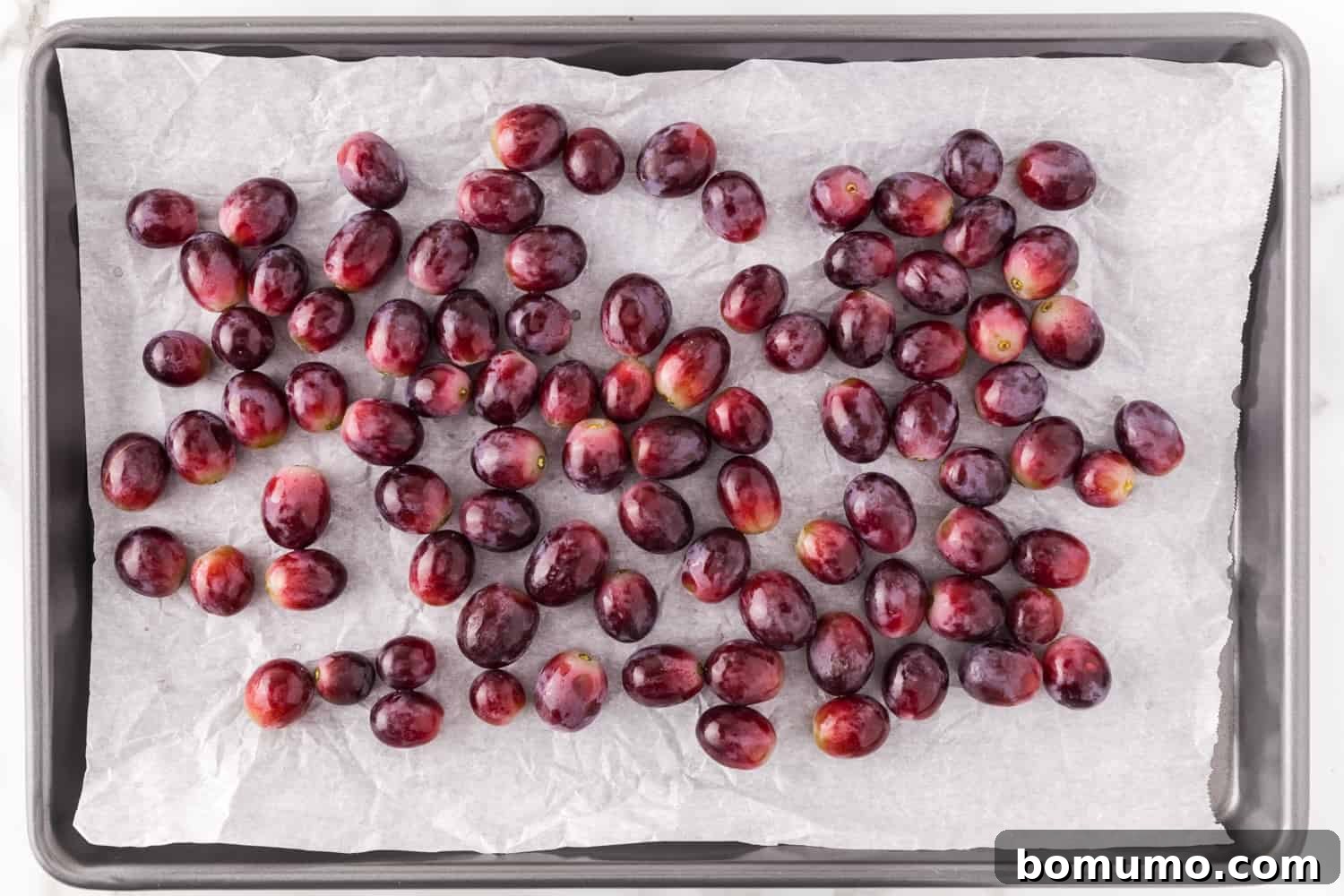 Fresh, plump red grapes arranged on a baking sheet, ready for roasting.