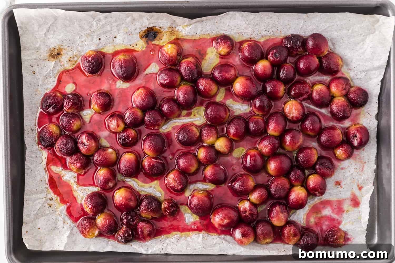 Beautifully roasted grapes, soft and slightly wrinkled, on a parchment-lined sheet pan after baking.