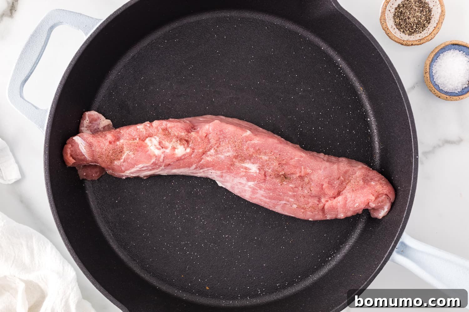 Raw pork tenderloin seasoned with salt and pepper, placed in a hot skillet before searing.