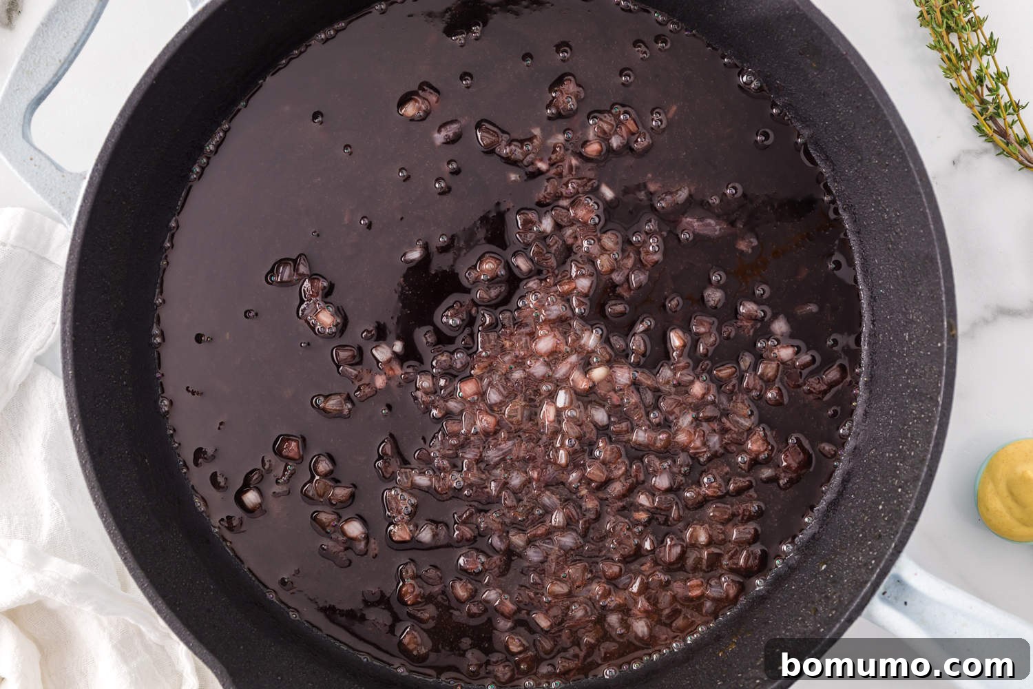 Finely diced shallots sautéing in an oven-safe skillet over medium heat.