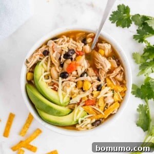 Chicken chili in a bowl garnished with avocado, cilantro, cheese.