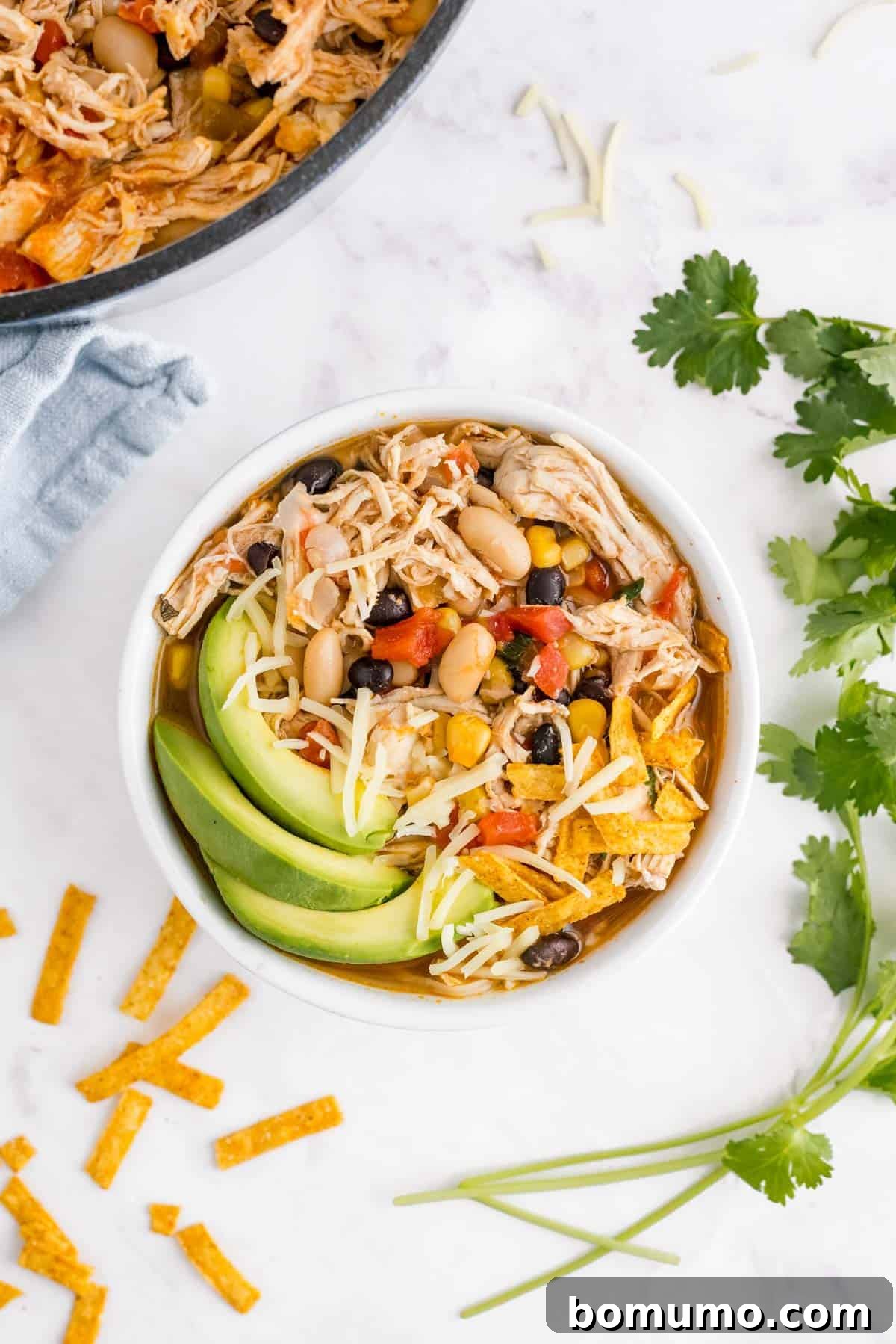 Chicken chili in a bowl with avocados, cilantro, and cheese.
