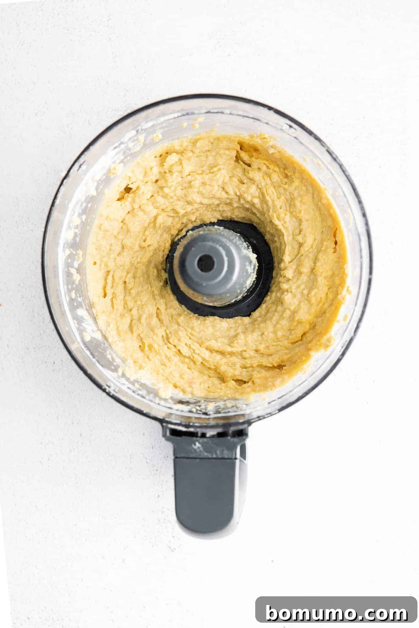 Overhead view of fully blended, creamy hummus swirling in a food processor, ready for seasoning and serving.