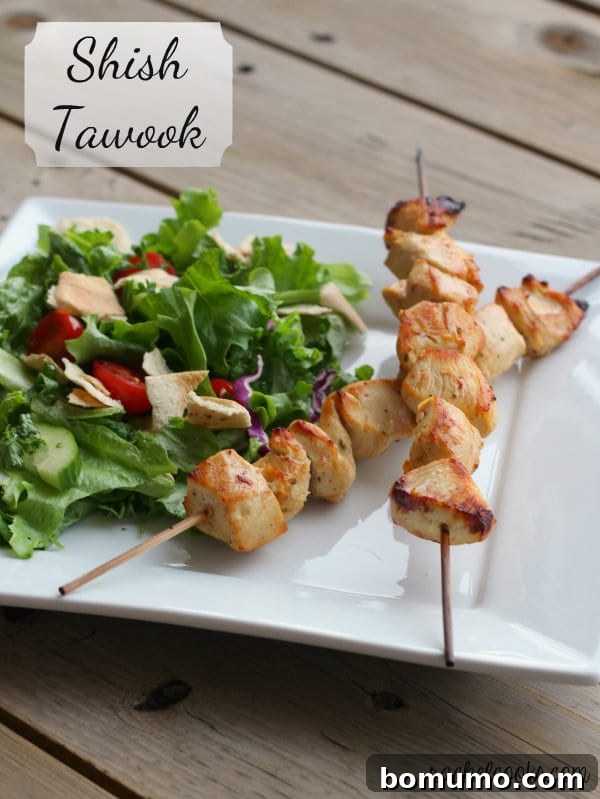 Two skewers with chicken and green salad on square white plate. Text overlay reads "Shish Tawook."