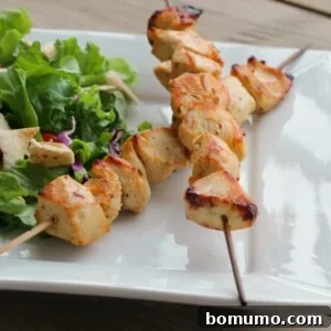 Two skewers with grilled chicken along with salad on square white plate.